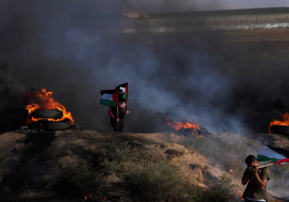 Палестинские демонстранты машут флагами и жгут шины во время протеста против израильского военного рейда в городе Дженин на Западном берегу реки Иордан вдоль забора на границе с Израилем, 3 июля 2023 года