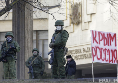 Неизвестные вооруженные люди в военной форме стоят возле плаката "Крым - это Россия" перед зданием парламента Автономной Республики Крым в Симферополе 1 марта 2014 года